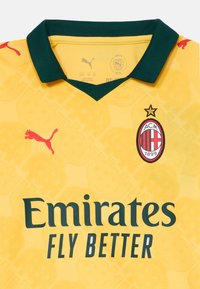 Gul fotballtrøye med grønn krage, AC Milan-crest, Puma-logo og sponsortekst "Emirates Fly Better".