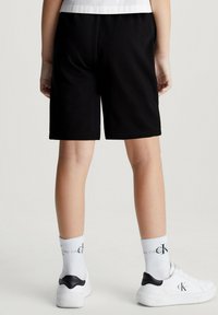 Pantaloni sportivi neri con una cintura elastica, che arrivano a metà coscia, abbinati a scarpe da ginnastica bianche e calze a righe.