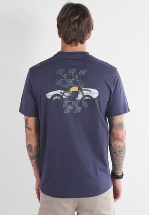 T-shirt en coton bleu marine avec un design graphique représentant une moto et une planche de surf, imprimé au dos. Manches courtes, coupe décontractée.