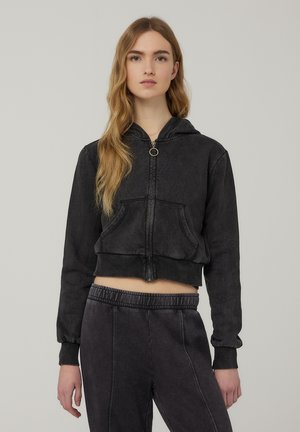 Felpa nera in denim cropped con zip frontale e anello di chiusura, caratterizzata da una tasca a marsupio e polsini a coste, abbinata a pantaloni felpati coordinati.