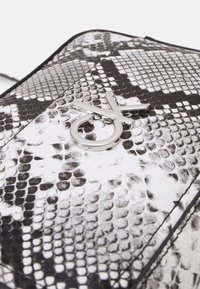 Černobílá kabelka s hadím potiskem a lesklou texturou, s kovovým logem ve stříbrné barvě umístěným na přední straně.