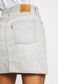 Jupe en denim gris à coupe classique, arborant une étiquette en cuir beige, un design de poche arrière signature et des détails de couture subtils.