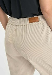 Beige corduroy broek met een ribbeltextuur, voorzien van een elastische tailleband en een bruine leren label aan de achterkant.