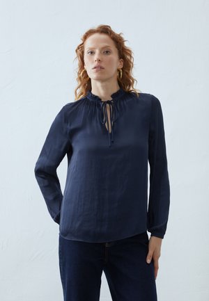 Marinblå bluse med lange ærmer, samlet halsudskæring med snorelukning, glat stof og en afslappet pasform, parret med mørk denim jeans.