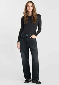 Top noir à manches longues associé à un pantalon en denim noir taille haute et large, doté de grandes poches avant et d'une ceinture. Texture lisse, design décontracté.