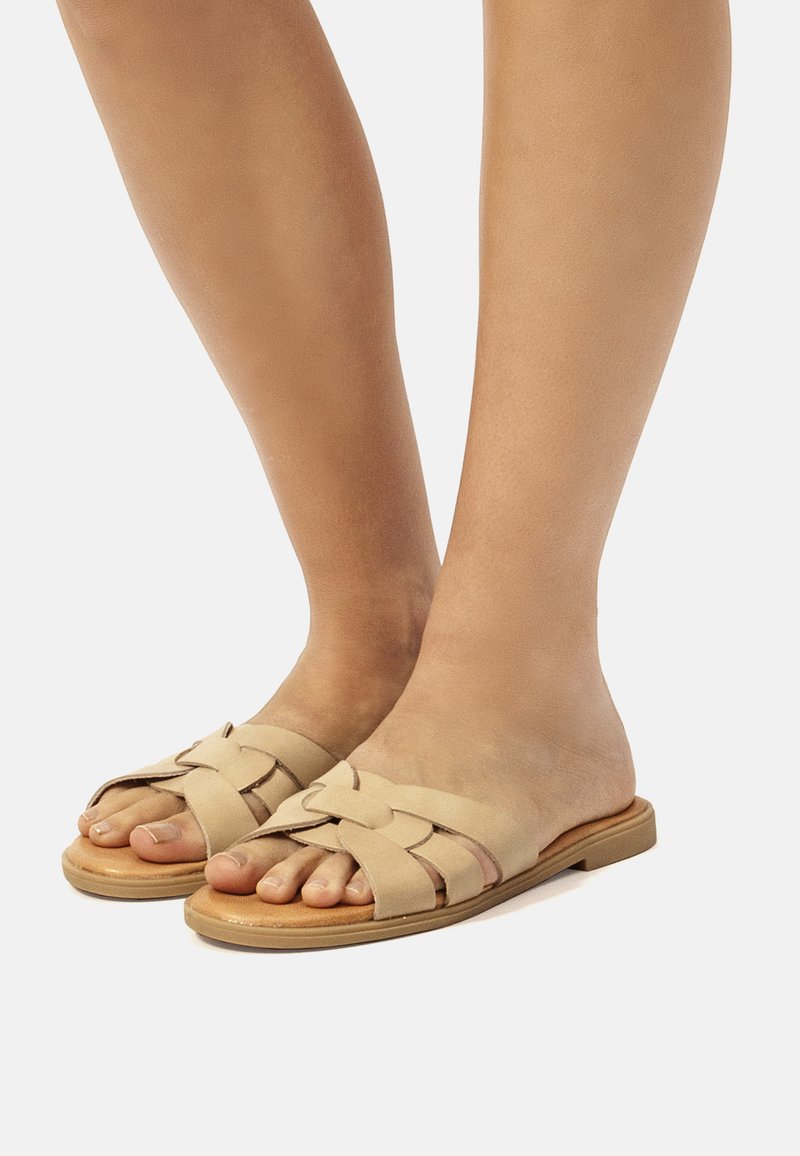 Sandales à glissière beiges avec une tige tissée, design à bout ouvert, semelle plate et détail de couture subtil, adaptées pour un usage décontracté.