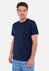 Navy blue cotton t-shirt with short sleeves, round neckline, and a patch pocket featuring a small blue logo detail.