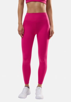 Leggings de talle alto fucsias hechos de una tela elástica, con una textura suave y un diseño ajustado. Combinados con zapatillas deportivas blancas.