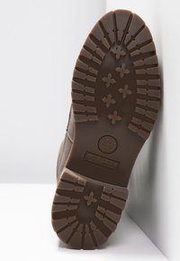 Timberland stövelsula, brun gummi med strukturerat mönster. Innehåller en cirkulär logotyp och upphöjda korsformer för grepp.