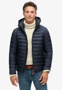 Marinen puffjakke i quiltet design med lynlås foran, har en hætte, sidelommer og elastiske manchetter, båret over en let sweater.