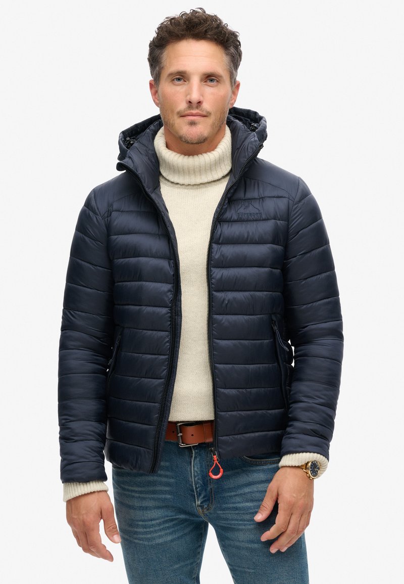 Marinen puffjakke i quiltet design med lynlås foran, har en hætte, sidelommer og elastiske manchetter, båret over en let sweater.