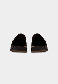Paire de chaussures noires sans lacets à petits talons vues de dos sur un fond clair uni.