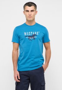 Turkusowa koszulka z krótkim rękawem z białym nadrukiem graficznym z tekstem oraz motywem konia, wykonana z mieszanki bawełny.