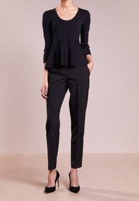 Černý peplum top s dlouhými rukávy, strukturovaná pletenina; spárováno s černými kalhotami na míru a černými vysokými podpatky.