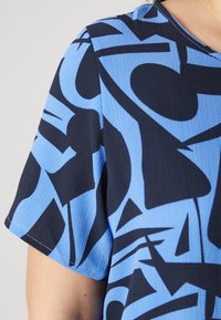Short-sleeve top featuring a blue and black abstract pattern on textured fabric. Round neckline with visible stitching and a relaxed fit.