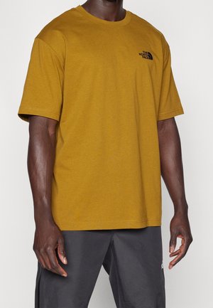 T-shirt en coton jaune moutarde, coupe décontractée, avec un petit logo noir sur le côté gauche de la poitrine et des manches courtes. Texture lisse.