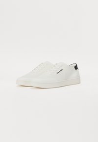 Adidași din plasă alba cu talpă din cauciuc, având branding embosat și un accent negru pe călcâi. Șireturi plate și un design cu vârf rotunjit.