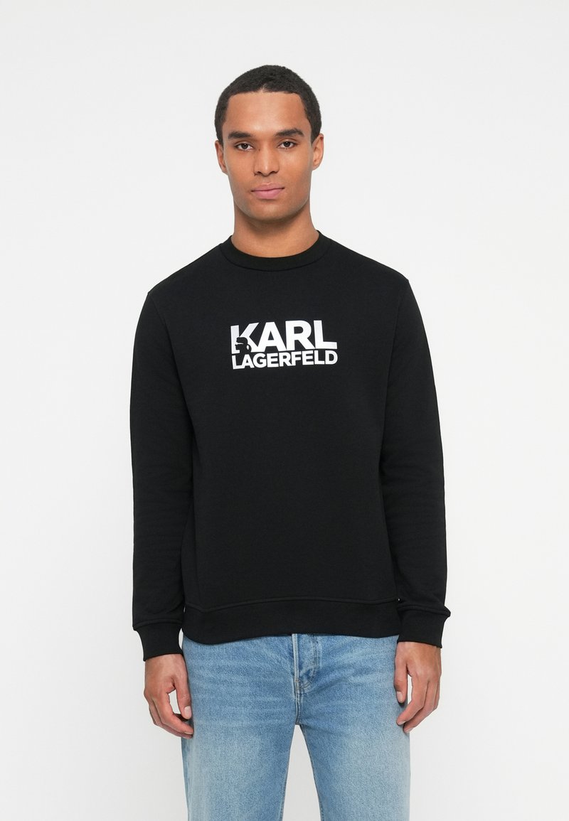 Sudadera negra con cuello redondo, puños acanalados y un audaz logo blanco de "Karl Lagerfeld" en la parte frontal. Ajuste casual y textura suave.