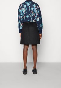 Pull en maille avec des motifs bleu foncé et floraux, associé à une jupe noire. Le modèle porte des chaussures noires. Focus sur le contraste des textiles et des couleurs.