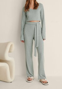 Conjunto de top corto de punto acanalado verde claro y pantalones de pierna ancha, que presenta una cintura con lazo, mangas largas y textura suave. Combinado con chanclas blancas.