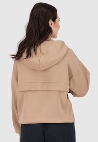 Felpa beige con un design della schiena a doppio strato, cappuccio regolabile e polsini a costine. Realizzata in tessuto morbido e liscio.