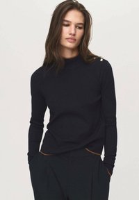 Black knit sweater with a high neckline, slim fit, and long sleeves. Features gold button detail on the shoulder and contrasting brown accents at the hems.