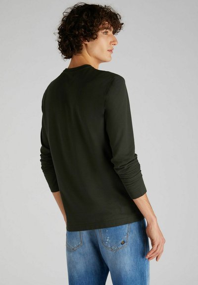 Camicia a maniche lunghe verde scuro con scollatura rotonda, tessuto morbido e maniche aderenti, abbinata a jeans chiari strappati azzurri.