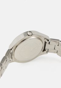 Montre en acier inoxydable argenté avec une finition polie, un boîtier rond et une couronne texturée. Dotée d'un bracelet maillon et d'un dos gravé.