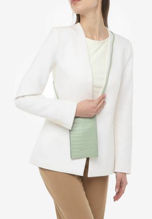 Mintgrøn crossover-taske med et struktureret krokodillemønster, rektangulær form, slank design og en lang rem, holdt i hånden mod en hvid blazer.