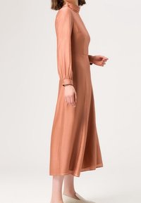 Langärmliges, knielanges Kleid aus weichem Pfirsichstoff mit einem taillierten Oberteil, hohem Ausschnitt und gerafften Bündchen. Glatte Textur, minimale Details.