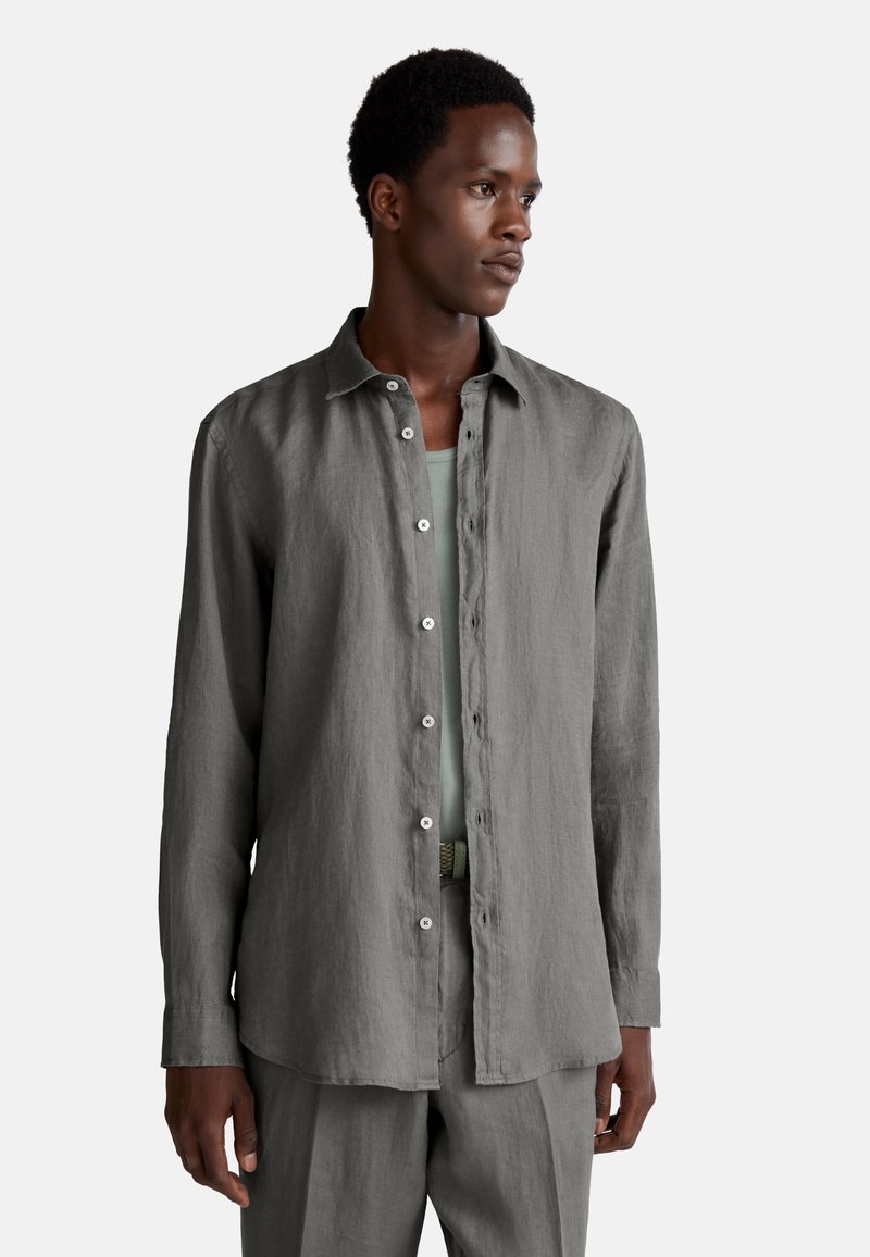 Chemise à manches longues en lin gris présentant un devant à boutons, une texture douce et une coupe décontractée, associée à une ceinture grise assortie et à un pantalon.