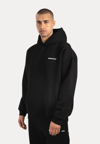 Felpa nera con tasca a marsupio frontale, polsini e orlo a costine. Presenta il logo "Smilbox Sport" in bianco sul petto. Tessuto di morbida consistenza.