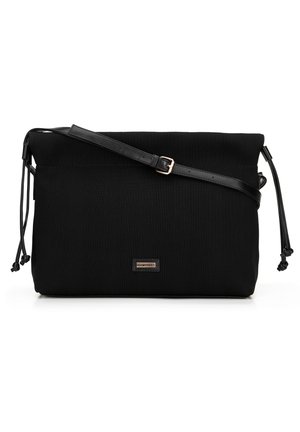 Black fabric crossbody bag with a textured surface, adjustable faux leather strap, drawstring closure, and a small front logo plate.