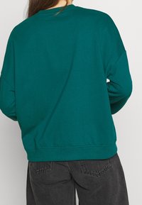 Felpa turchese con scollatura rotonda, vestibilità ampia e polsini e orlo a coste. Realizzata in un tessuto morbido, presenta una texture liscia e un design minimalista.