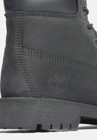 Bota de cuero gris con un acabado texturizado, que presenta costuras prominentes, una suela resistente y un logotipo en relieve en el lateral.