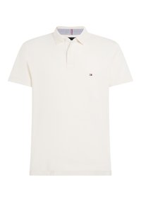 Bomullspolo i off-white med knäppning i tre knappar, korta ärmar och en liten logotyp på bröstet. Horisontellt randigt inre krage.