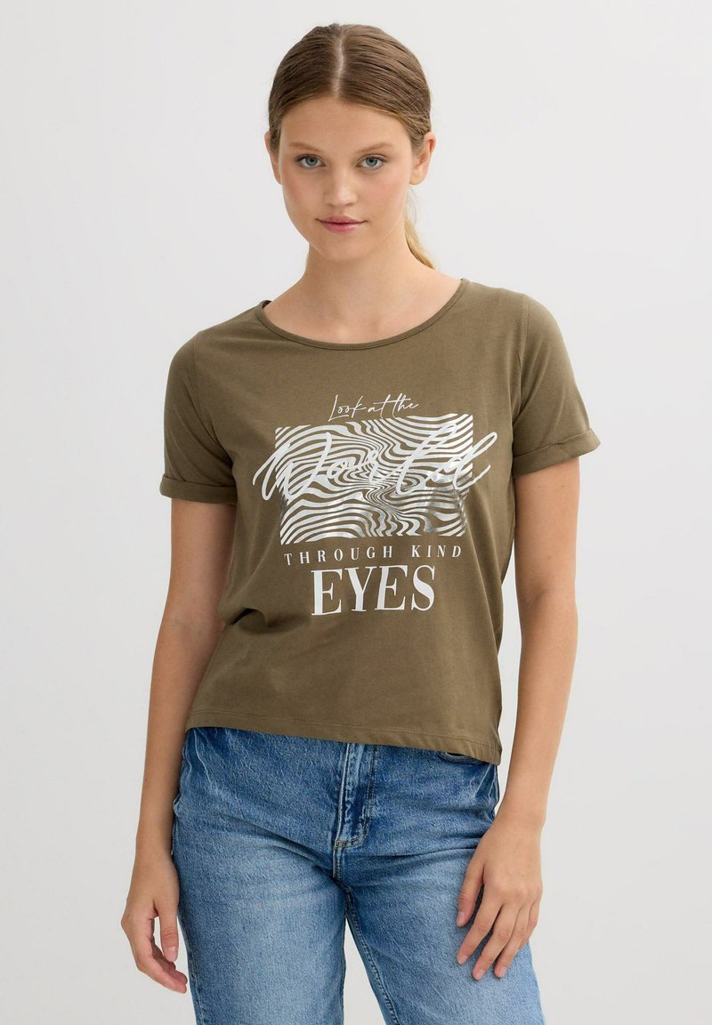 Camiseta verde oliva de mangas cortas enrolladas y escote redondo. Presenta texto gráfico en blanco y líneas onduladas. Material de algodón suave.