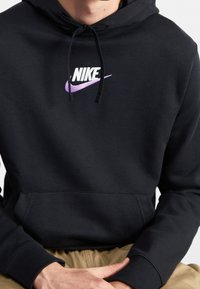 Svart Nike-hoodie med lila logotyp. Har dragsko i huvan, känguruficka och ribbade muddar. Mjuk tygstruktur.
