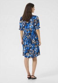 Bloemenjurk met blauwe, bruine en witte patronen; korte puffmouwen; geplooide rok; gemaakt van lichtgewicht stof; gedragen met haksandalen.
