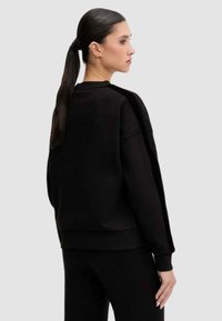 Felpa nera oversize con polsini e orlo a coste. Tessuto liscio con dettagli di design minimali, stile con scollo tondo.