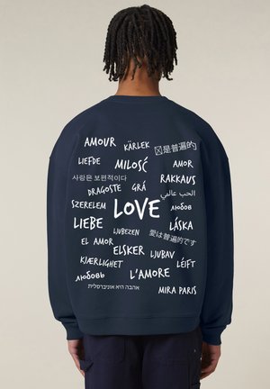 Donker marineblauwe sweatshirt met een ronde hals, met witte tekst in verschillende talen die "liefde" voorstellen in een verspreide lay-out op de achterkant.