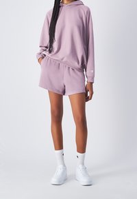 Felpa viola chiaro con una vestibilità comoda, abbinata a pantaloni corti coordinati. Sneakers bianche e calzini con dettagli del logo completano l'outfit.