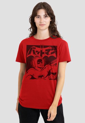 Young woman with long wavy hair wearing a red T-shirt featuring a black Batman graphic and Japanese characters on a light gray background.