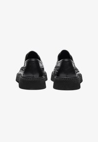 Chaussures noires en cuir avec une finition lisse, tissage texturé sur les côtés et une épaisse semelle en caoutchouc noir. Talon aplati, design minimaliste.