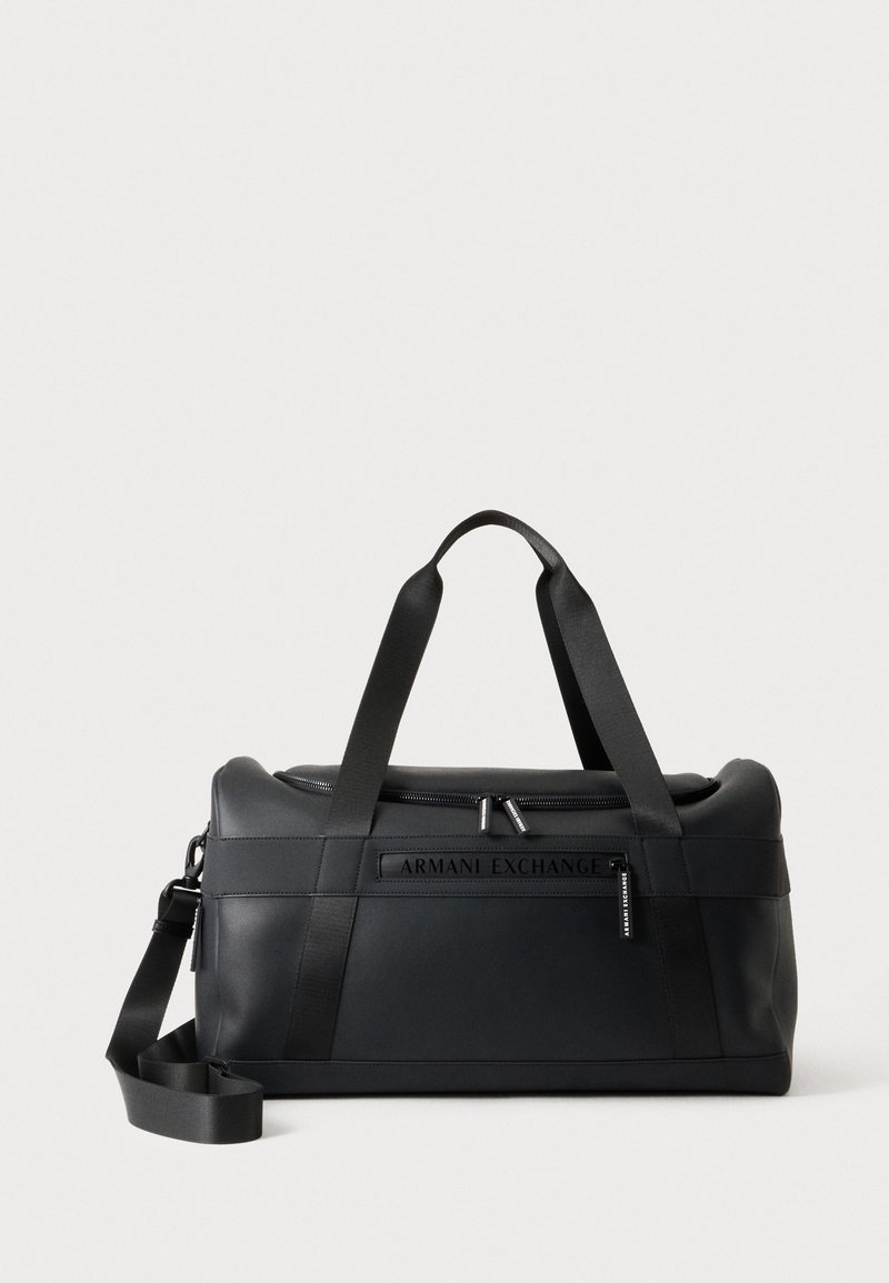 Черна спортна чанта Armani Exchange с горни дръжки, сваляща се презрамка за рамо и основно отделение с цип на светъл фон.