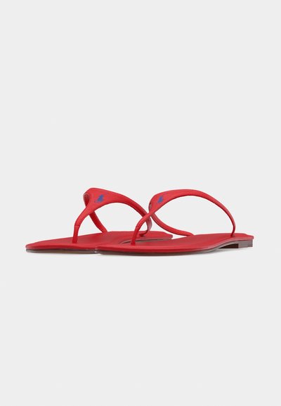 Sandales plates rouges en forme de tongs avec des brides fines et un logo brodé bleu sur chaque bride, présentées sur un fond blanc.