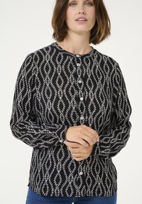 Blusa nera a bottoni con un motivo a foglie bianche e onde, scollatura rotonda, maniche lunghe e una leggera trama.