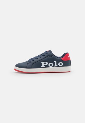 Marineblå sneaker med hvid tekst "Polo" på siden, rød hælkappe, hvid mellemsål og rød ydersål, vist fra ydersiden.