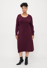 Burgundy long-sleeve dress with a round neckline and a straight cut. Smooth fabric, mid-calf length, paired with black ankle boots.