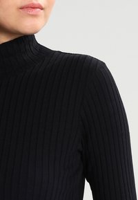 Svart ribbad polotröja med hög krage och vertikal textur, tillverkad av ett mjukt, stretchigt material för en åtsittande passform.